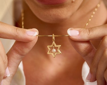 May include: A gold necklace with a star of David pendant featuring a small pearl in the center.