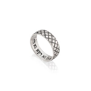 Puede incluir: Un anillo de plata con un patrón de diamante texturizado en la banda. El interior de la banda está inscrito con texto hebreo.