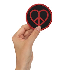 May include: A black and red embroidered patch with a peace sign inside a heart shape.