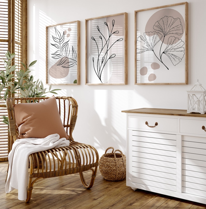 Peut inclure: Un meuble blanc avec deux tiroirs et deux portes, un fauteuil en osier avec un coussin brun et une couverture blanche, et trois impressions encadr&eacute;es avec des dessins au trait noirs de feuilles et de branches sur un mur blanc.