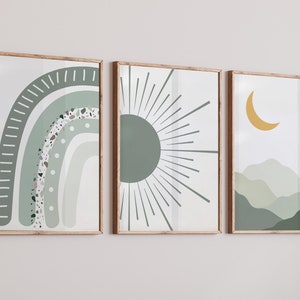 May include: Three framed prints with abstract designs in shades of green and yellow. The first print features a green and white rainbow with a speckled texture. The second print features a green sun with radiating lines. The third print features a yellow crescent moon and green hills.