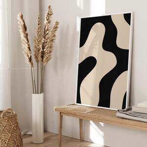 May include: A black and beige abstract art print in a white frame hangs above a wooden bench with a woven seat. Dried pampas grass is in a white vase on the floor.