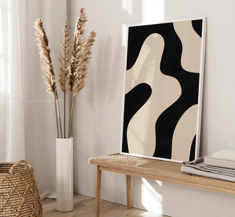 May include: A black and beige abstract art print in a white frame hangs above a wooden bench with a woven seat. Dried pampas grass is in a white vase on the floor.