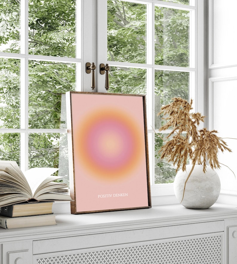 May include: A framed print with a pink and orange gradient circle design. The text "POSITIV DENKEN" is printed in white at the bottom of the print.