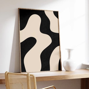 May include: A framed abstract print with a black and beige color scheme. The print features a series of organic shapes that resemble waves or clouds. The print is hanging on a white wall above a wooden desk with a chair.