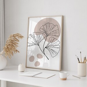 Peut inclure: Une impression encadr&eacute;e avec un design minimaliste mettant en sc&egrave;ne une illustration stylis&eacute;e en noir et blanc de feuilles de ginkgo sur un fond rose poudr&eacute;.