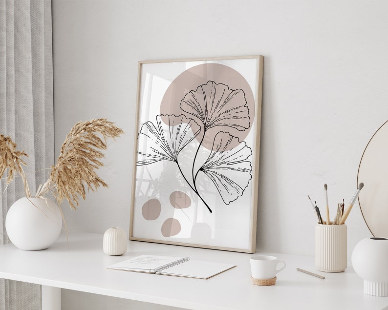 Peut inclure: Une impression encadr&eacute;e avec un design minimaliste mettant en sc&egrave;ne une illustration stylis&eacute;e en noir et blanc de feuilles de ginkgo sur un fond rose poudr&eacute;.