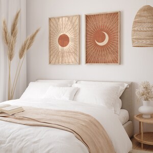 Puede incluir: Dos impresiones enmarcadas con un dise&ntilde;o minimalista. Las impresiones presentan un sol y una luna creciente sobre un fondo terracota con l&iacute;neas blancas que irradian hacia afuera.