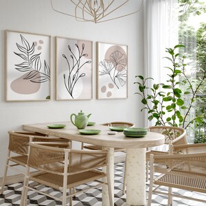 Peut inclure: Une salle &agrave; manger avec une table en bois et six chaises. La table a une finition en bois clair et les chaises sont en osier tress&eacute;. Il y a trois impressions encadr&eacute;es sur le mur derri&egrave;re la table, chacune repr&eacute;sentant un dessin au trait diff&eacute;rent d'une plante. Les impressions sont dans un style minimaliste avec un fond rose clair.