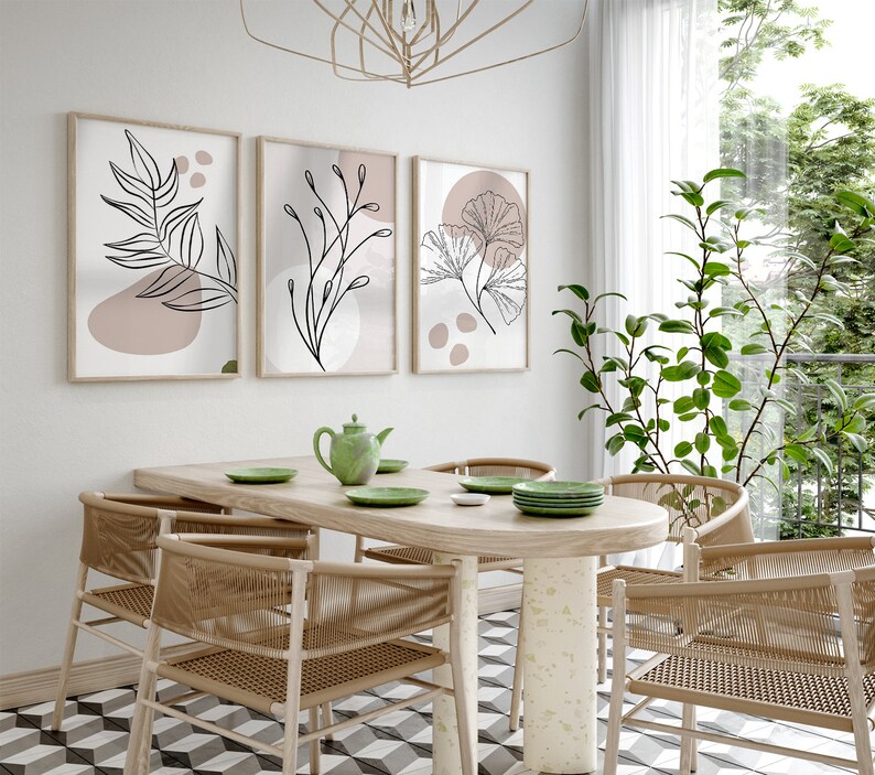 Peut inclure: Une salle &agrave; manger avec une table en bois et six chaises. La table a une finition en bois clair et les chaises sont en osier tress&eacute;. Il y a trois impressions encadr&eacute;es sur le mur derri&egrave;re la table, chacune repr&eacute;sentant un dessin au trait diff&eacute;rent d'une plante. Les impressions sont dans un style minimaliste avec un fond rose clair.