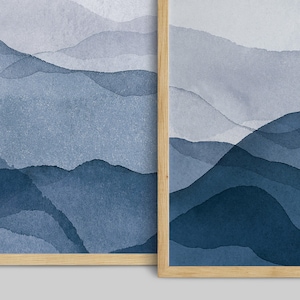 May include: Two framed abstract watercolor paintings with a blue and gray color scheme. The paintings depict a landscape of mountains and hills.