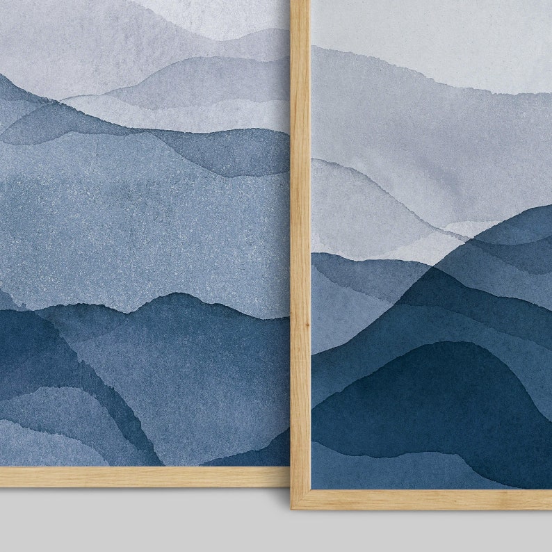 May include: Two framed abstract watercolor paintings with a blue and gray color scheme. The paintings depict a landscape of mountains and hills.