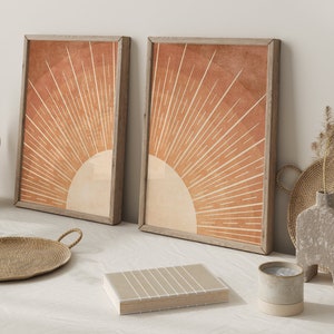 Op de afbeelding: Twee ingelijste prints met een minimalistisch zonnestralenontwerp in tinten oranje en bruin. Het zonnestralenontwerp is gecentreerd in elke print en heeft een witte achtergrond.