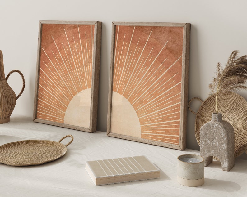 Op de afbeelding: Twee ingelijste prints met een minimalistisch zonnestralenontwerp in tinten oranje en bruin. Het zonnestralenontwerp is gecentreerd in elke print en heeft een witte achtergrond.