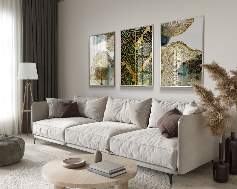 Puede incluir: Tres impresiones de arte abstracto enmarcadas con acentos dorados y verdes. Las impresiones presentan un dise&ntilde;o circular con una textura de veta de madera. Las impresiones est&aacute;n colgadas en una pared blanca sobre un sof&aacute; blanco.