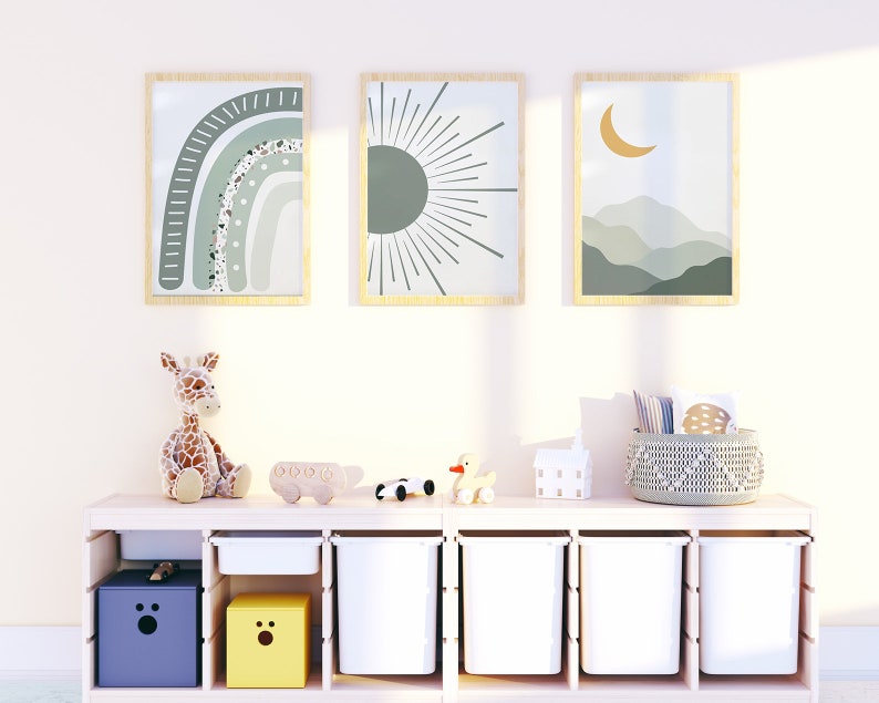 May include: A white shelf unit with six cubbies, two of which are filled with yellow and purple boxes. The other cubbies are empty. There are three framed prints on the wall above the shelf unit, featuring a rainbow, a sun, and a crescent moon. A stuffed giraffe, a toy car, and a toy duck are on the shelf.