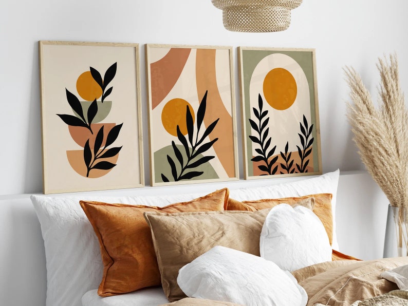 Op de afbeelding: Drie abstracte kunstprints met een minimalistisch ontwerp met zwarte silhouetten van bladeren en takken tegen een achtergrond van beige, groen en oranje.