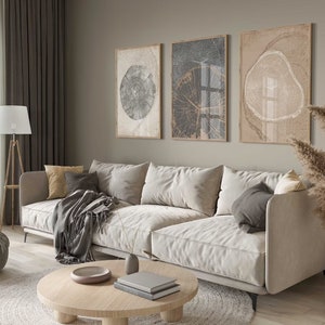 Könnte beinhalten: Ein hellgraues Ecksofa mit drei Kissen, einer grauen Wolldecke und einem Holz-Couchtisch mit Büchern und einer Schale darauf. Das Sofa steht in einem Wohnzimmer mit einem großen Fenster, braunen Vorhängen und drei gerahmten Drucken an der Wand.