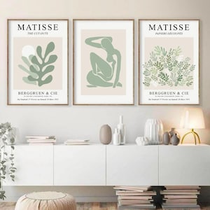 May include: Three framed art prints with a minimalist design featuring green and white abstract shapes. The prints are titled "Matisse The Cut-Outs", "Matisse Papiers Decoupes", and "Berggruen & Cie".