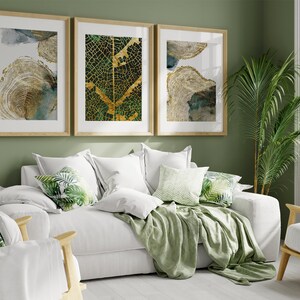 Puede incluir: Un sof&aacute; blanco con mantas y almohadas verdes con un patr&oacute;n de hojas tropicales. Tres impresiones de arte abstracto enmarcadas con acentos dorados y verdes cuelgan de una pared verde salvia detr&aacute;s del sof&aacute;.