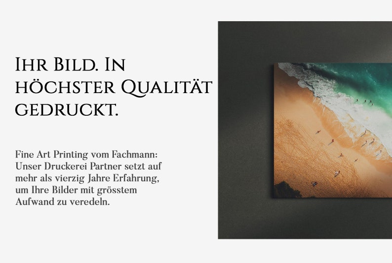 May include: A framed photograph of a beach scene with turquoise water, white waves, and a sandy beach with people walking on it. The text "IHR BILD. IN H&Ouml;CHSTER QUALIT&Auml;T GEDRUCKT." is printed below the image.