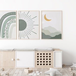 May include: Three framed prints with abstract designs in shades of green and yellow. The prints feature a rainbow, a sun, and a crescent moon over a mountain range. The prints are hanging on a white wall above a wooden storage bench with three compartments.
