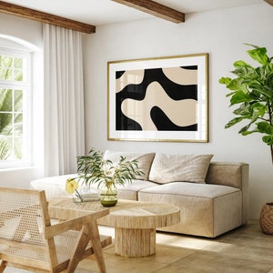 May include: A living room with a beige sectional sofa, a wooden coffee table, and a large framed abstract print with black and beige shapes. A potted plant with green leaves is in the corner of the room.