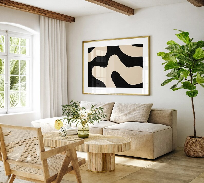 May include: A living room with a beige sectional sofa, a wooden coffee table, and a large framed abstract print with black and beige shapes. A potted plant with green leaves is in the corner of the room.