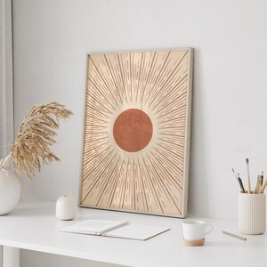 Puede incluir: Una impresi&oacute;n enmarcada de un dise&ntilde;o de sol minimalista con un c&iacute;rculo rojo-naranja y l&iacute;neas radiantes de color beige.