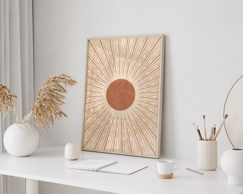Puede incluir: Una impresi&oacute;n enmarcada de un dise&ntilde;o de sol minimalista con un c&iacute;rculo rojo-naranja y l&iacute;neas radiantes de color beige.