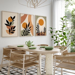 Op de afbeelding: Een eetkamer met een tafel van licht hout en zes stoelen. De stoelen zijn gemaakt van gevlochten riet en hebben een natuurlijke bruine kleur. Er hangen drie abstracte kunstprints aan de muur achter de tafel. De prints tonen geometrische vormen en bladeren in tinten bruin, oranje en groen.