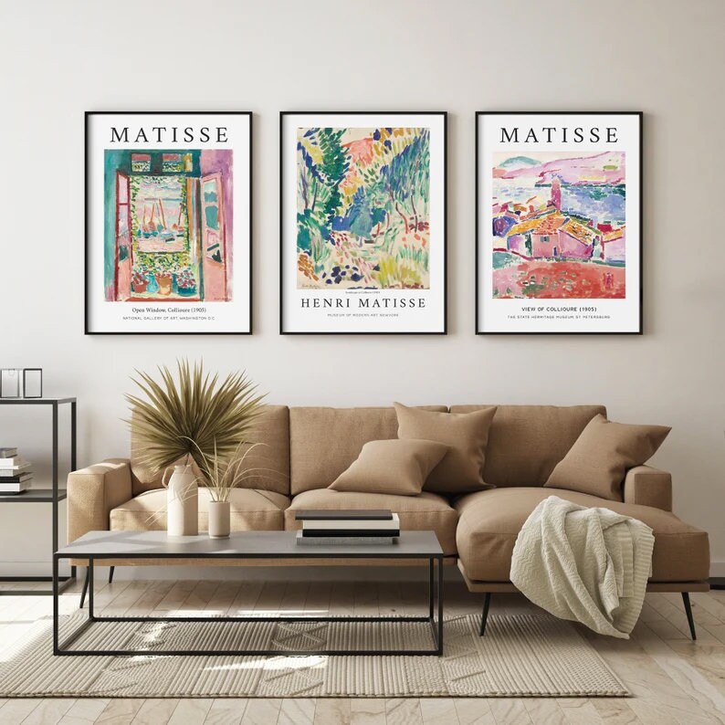 May include: Three framed art prints of paintings by Henri Matisse. The prints are titled "Open Window, Collioure (1905)", "Henri Matisse" and "View of Collioure (1905)". The prints are hanging on a white wall above a brown couch.