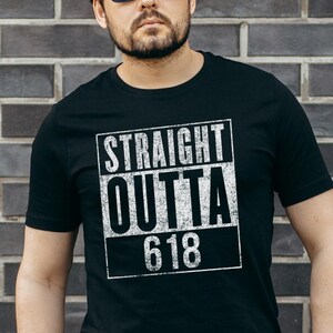 May include: Black t-shirt featuring the text "STRAIGHT OUTTA 618" in a white, distressed font. The graphic is in a rectangular box. The shirt has a crew neck.