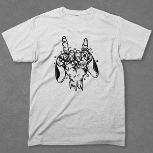 Pu&ograve; includere: Una maglietta bianca con un'illustrazione in bianco e nero di una mano che tiene due controller per videogiochi. La mano sta facendo un gesto rock and roll.