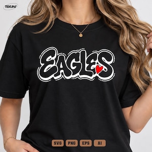 Puede incluir: Una camiseta negra de manga corta con la palabra EAGLES en una fuente de estilo grafiti negra con borde blanco en el pecho. Un pequeño corazón rojo sólido está colocado junto a la letra S. El texto TEKUN es visible en la esquina superior.