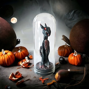 Peut inclure: Une figurine de créature noire et rouge est enfermée dans un dôme de verre. Le dôme repose sur une surface en bois avec des citrouilles et d'autres décorations d'automne.