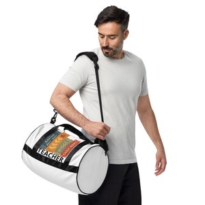May include: White duffel bag with a black strap. The bag has a colorful design of stacked books with the words "Baking", "Cozy Home", "Hygge", and "Teacher" on the front.