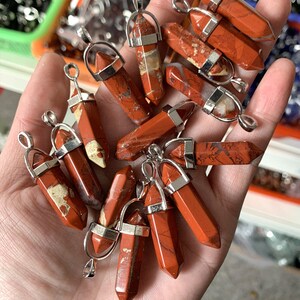 May include: A collection of red jasper stone pendants with silver-toned metal bails. The stones are all different shapes and sizes, but they are all polished and have a smooth finish.