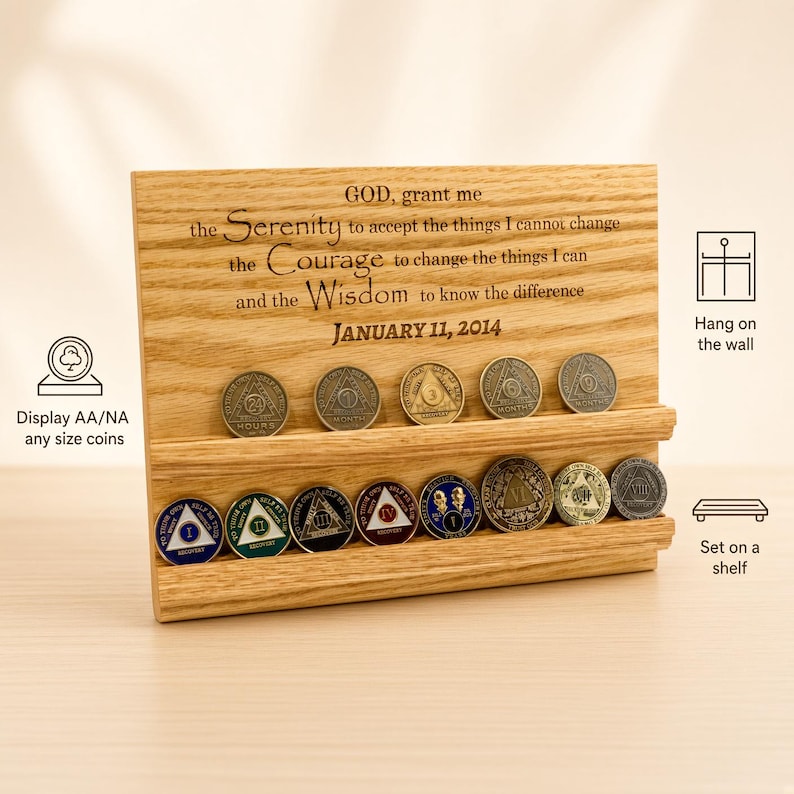 May include: A rectangular light-colored wooden display stand with two horizontal grooves for holding coins. The wood is engraved with the Serenity Prayer and the date January 11, 2014. Several circular metal recovery coins are placed in the grooves.