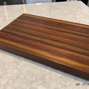 May include: A large, rectangular wooden cutting board with a rich brown and dark brown striped pattern. The board measures 11" x 17" x 1-1/2".