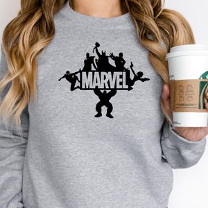 May include: Gray sweatshirt with a black silhouette of Marvel characters, including Hulk, Thor, Iron Man, and Spider-Man, with the word "MARVEL" in white letters.