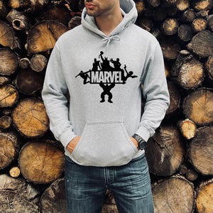 May include: A gray hooded sweatshirt with a black graphic print of Marvel superheroes. The graphic features the Marvel logo and silhouettes of several superheroes, including Iron Man, Captain America, Thor, and Hulk.