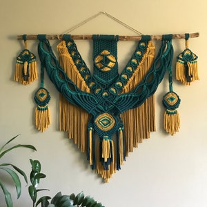 May include: A green and gold macrame wall hanging with a geometric pattern and fringe. The hanging is made with natural fibers and has a bohemian style.