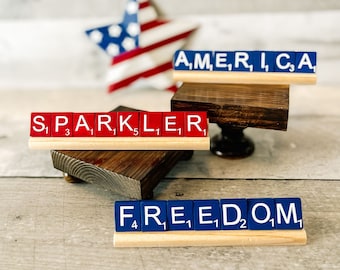 May include: Red, white, and blue star-shaped decoration with the words "AMERICA", "SPARKLER", and "FREEDOM" spelled out using letter tiles on wooden blocks.