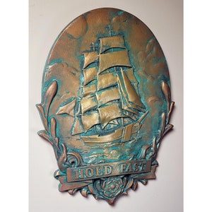 May include: A bronze-colored oval wall plaque with a raised image of a sailing ship with a banner that reads "HOLD FAST". The plaque has a green patina finish.