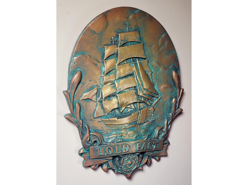 May include: A bronze-colored oval wall plaque with a raised image of a sailing ship with a banner that reads "HOLD FAST". The plaque has a green patina finish.