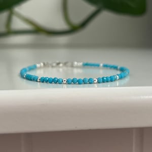 May include: A delicate turquoise beaded bracelet with silver accents. The bracelet features small, round turquoise beads and interspersed silver beads. The clasp is also silver. The bracelet is displayed on a white surface.