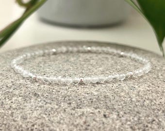 May include: A delicate bracelet made of clear quartz beads and silver accents. The bracelet is on a gray stone background.