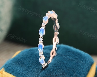 May include: A delicate rose gold band with a row of moonstone and diamond accents. The ring is displayed in a blue velvet ring box.