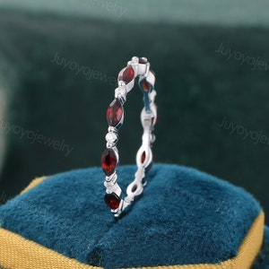 May include: A delicate eternity band featuring a row of red gemstones and small diamonds set in a white metal band.